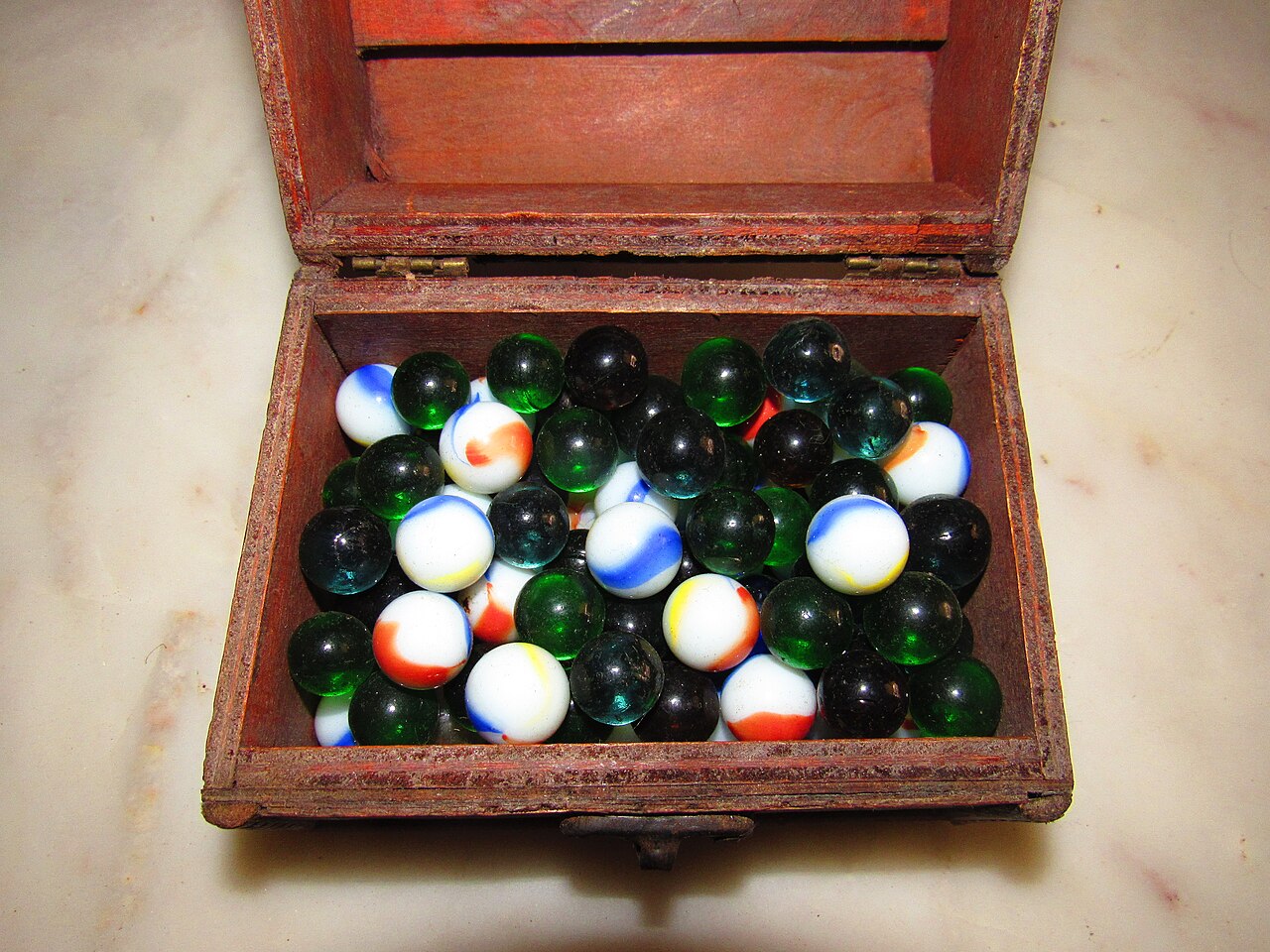 Treasure chest full of green, black and swirled white glass marbles